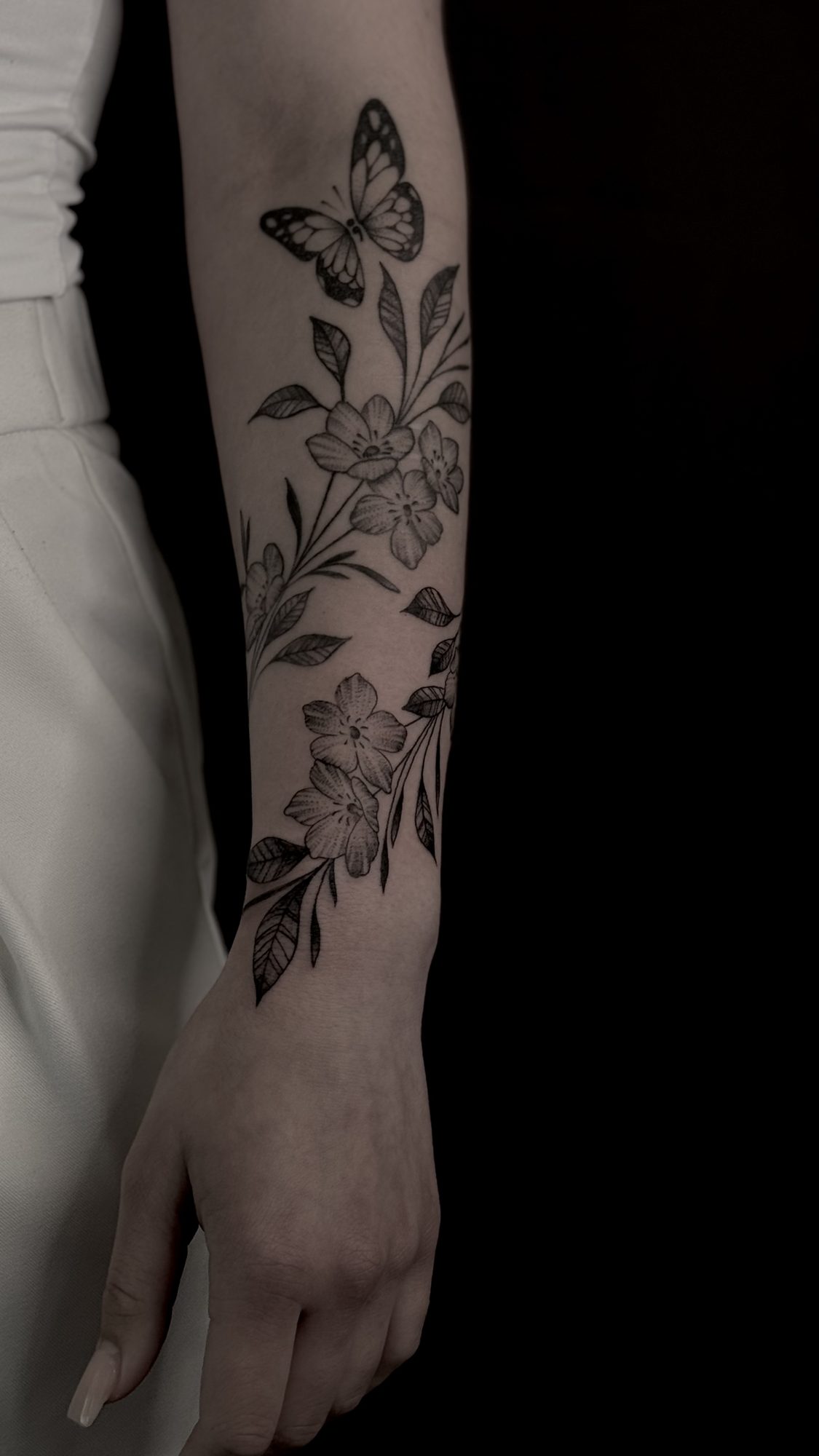 Blütenranke mit Schmetterling am Unterarm, Blackwork Tattoo von Andre bei Eine Liebe Tätowiergeschäft in Bochum