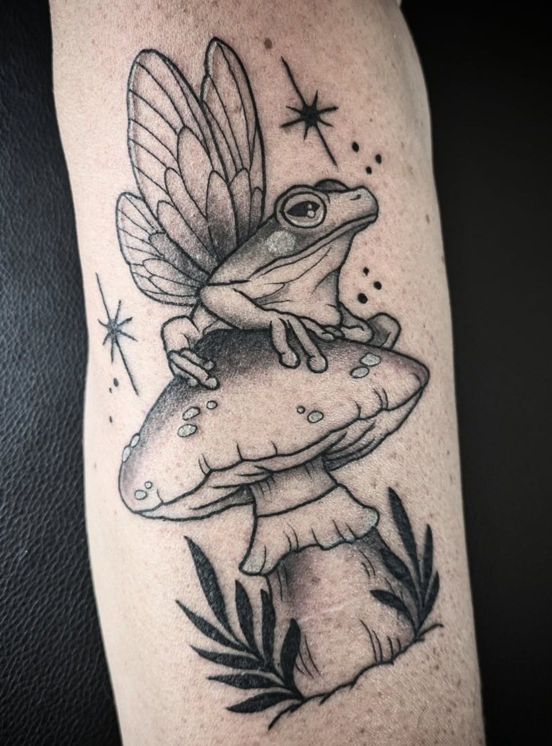 Frosch mit Feenflügeln auf Pilz am Unterarm, Blackwork Tattoo von Melissa bei Eine Liebe Tätowiergeschäft in Bochum