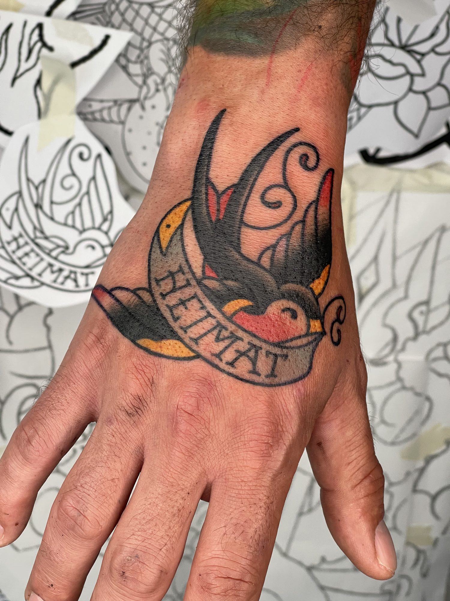 Schwalbe mit Heimat-Banner auf der Hand, Hand Tattoo von Salle bei Eine Liebe Tätowiergeschäft in Bochum